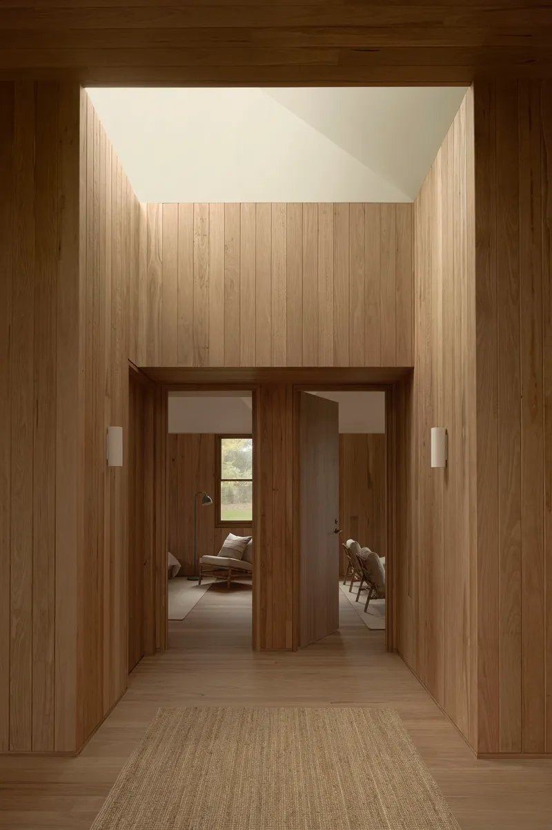 Entry hall framed by timber walls beneath a recessed skylight with paired doorways beyond