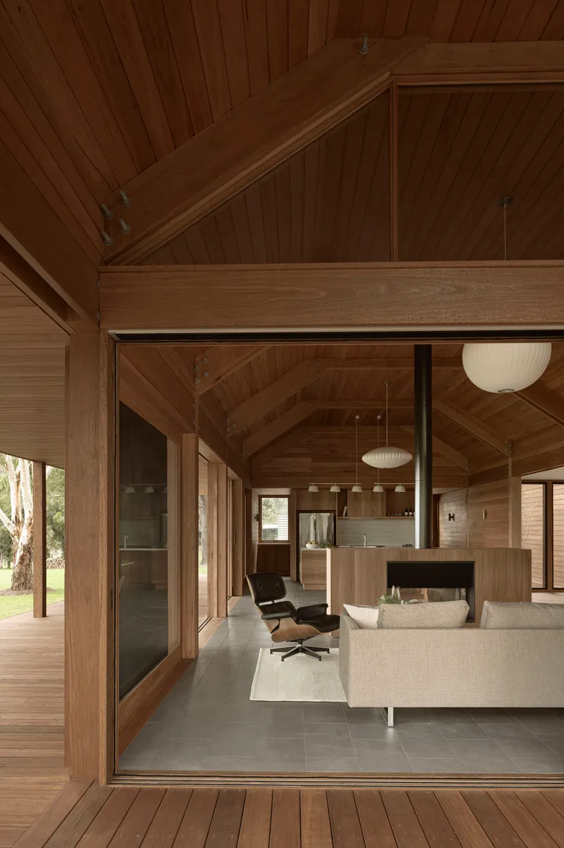 Open-plan living area with exposed timber beams and glazed doors connecting to the exterior deck
