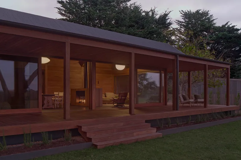 Glazed timber veranda with exposed posts and corrugated metal roof overlooking lawn at twilight