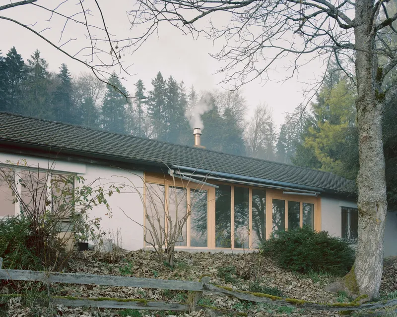 Exterior view of the low-pitched roof with chimney smoke rising into the forest mist