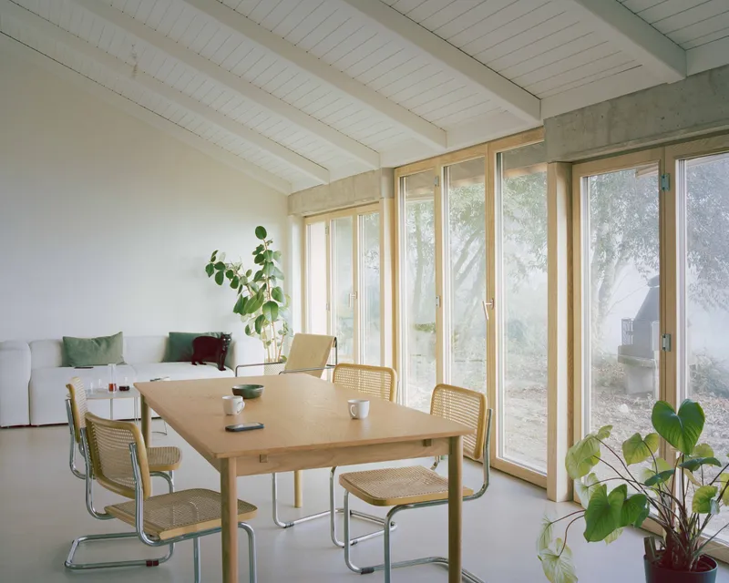 Dining area with timber-framed glazing and exposed concrete beam beneath a white planked ceiling