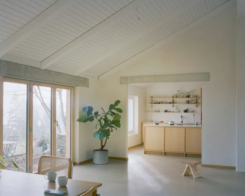 Living space with exposed concrete beam framing a view through to the kitchen in soft daylight