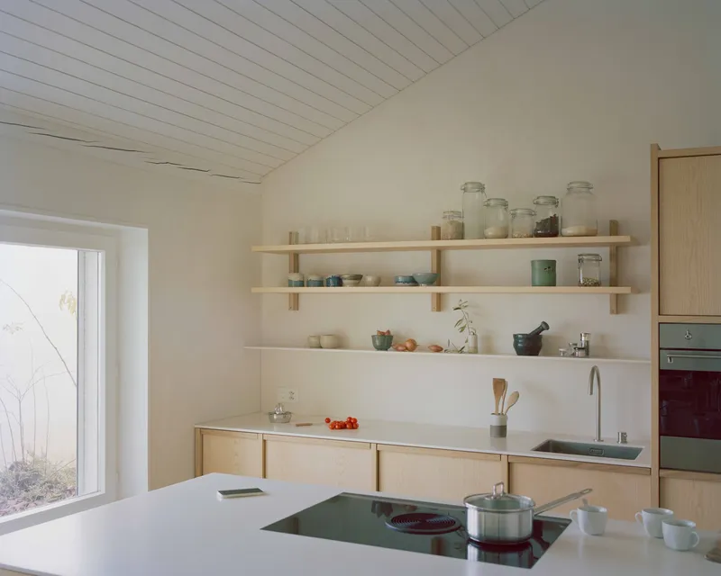 Kitchen counter with island cooktop and open timber shelving under a sloped white plank ceiling