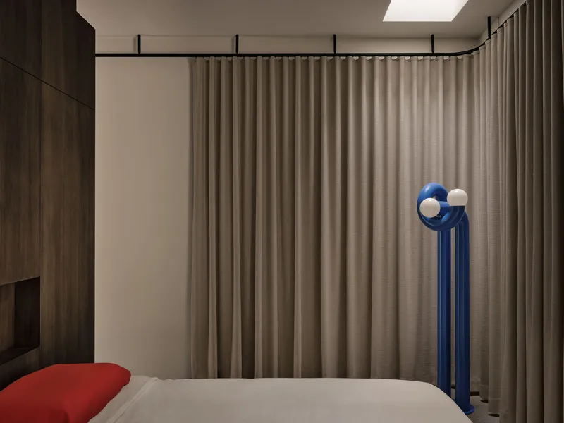 Bedroom corner showing blue sculptural lamp beside bed with timber joinery and draped ceiling track