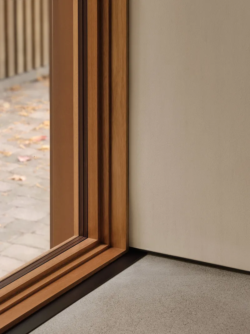 Detail of timber window frame meeting plastered wall corner with autumn leaves visible outside