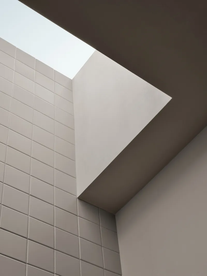 Upward view of a skylight between white tiled wall and angled plaster ceiling planes