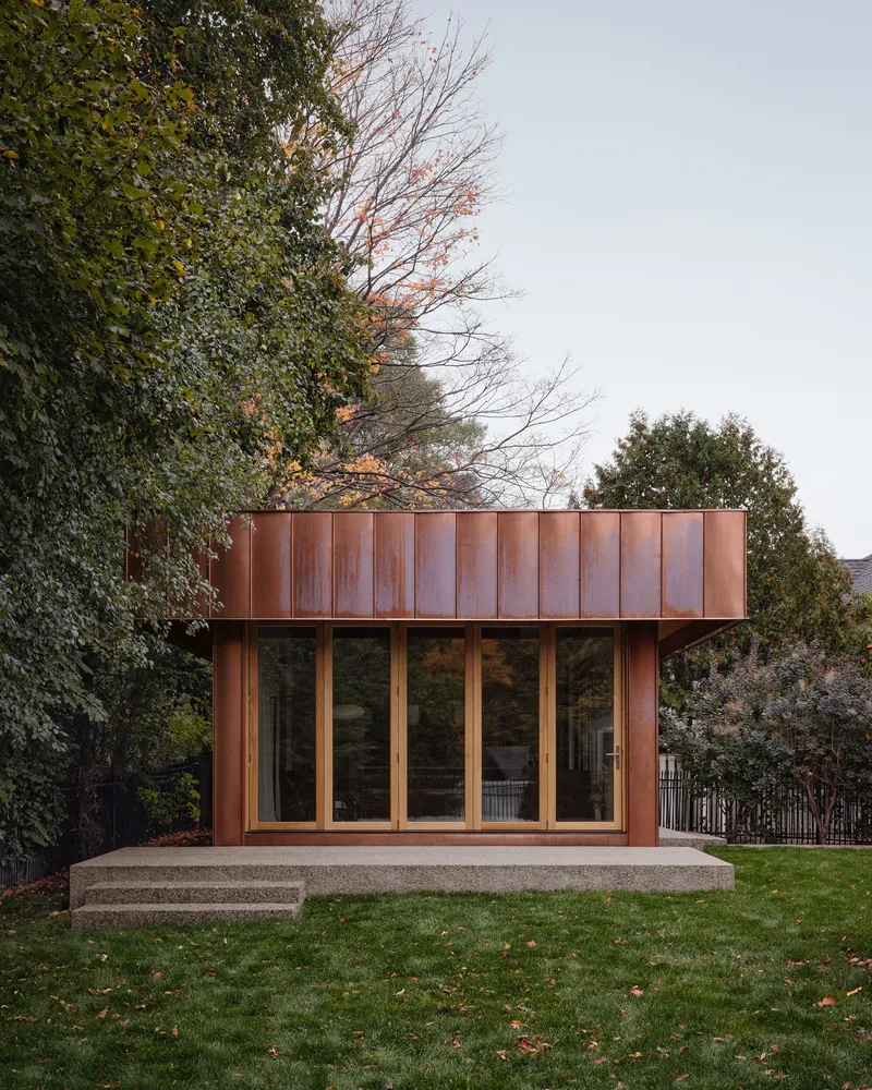 Freestanding structure with weathered copper panels and glazed facade on stepped concrete base