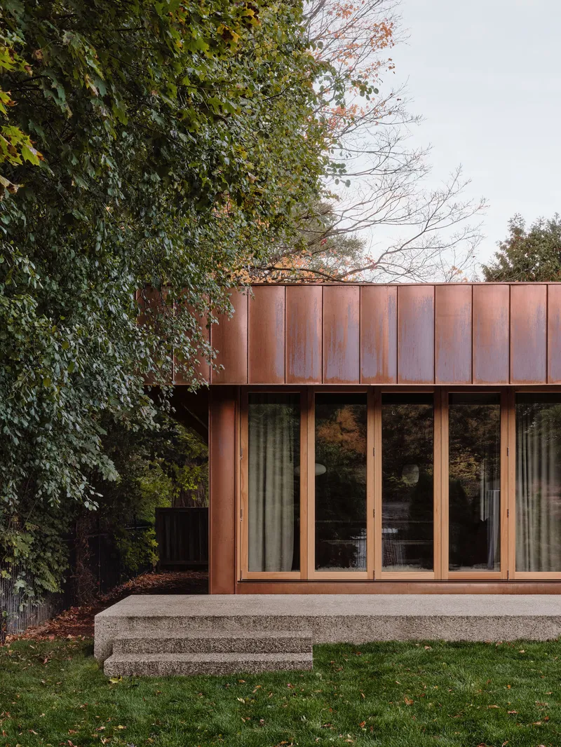 Corner detail of copper-clad volume with folding glass doors and adjacent ivy-covered wall