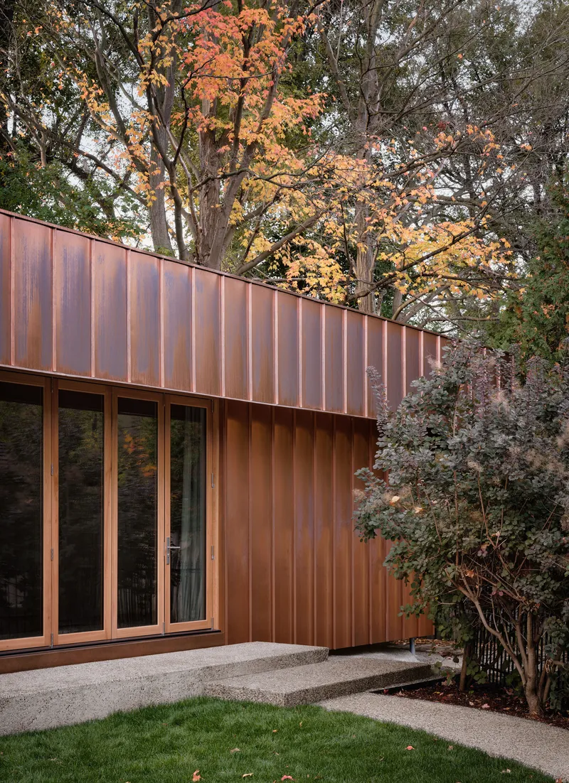 Copper facade with vertical joint detailing beneath trees showing autumn foliage
