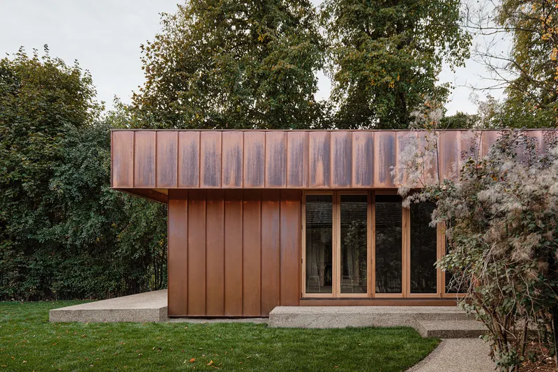 Garden pavilion with weathered copper cladding and glazed doors surrounded by lawn and mature trees
