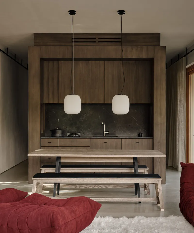 Kitchenette with timber cabinetry and dark stone backsplash framed by dining table with benches