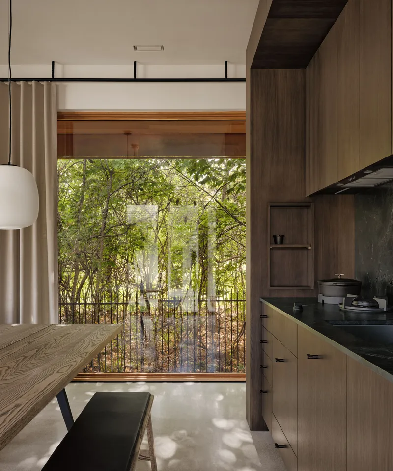 Kitchen with timber cabinetry and large window framing a view of lush vegetation beyond balcony railing