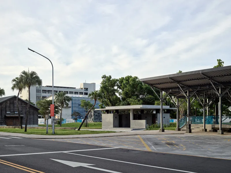 Street view of the concrete pavilion with adjacent steel and timber canopy structure at dusk