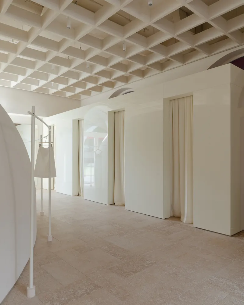 Interior corridor with coffered ceiling grid and pale vertical-plank doors set in curved white walls