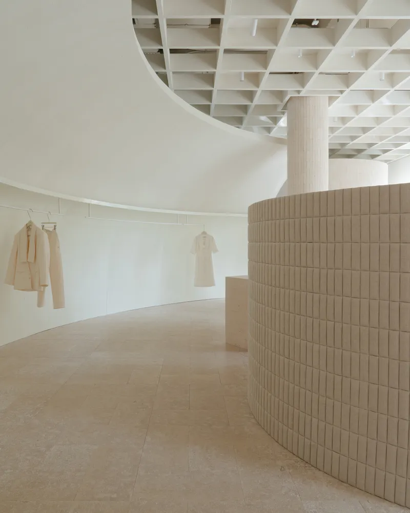 Curved retail wall clad in ribbed timber tiles beneath a coffered ceiling with garments on display