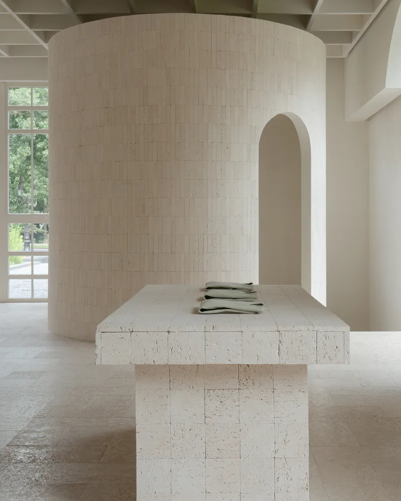 Textured limestone block table beside a curved cylindrical wall with an arched doorway in soft daylight