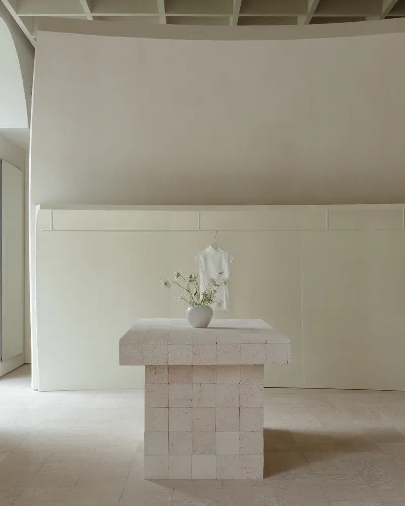 Travertine pedestal table with a vase of white flowers beneath a coffered ceiling and paneled wall