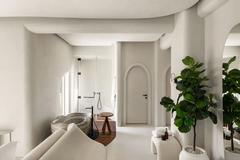 Open bathroom with carved stone tub on timber platform, arched doorways and fiddle-leaf fig trees