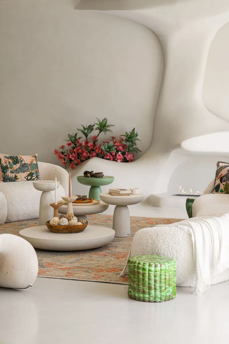 Living room with sculptural plaster walls and low seating arranged around pedestal tables on patterned rug