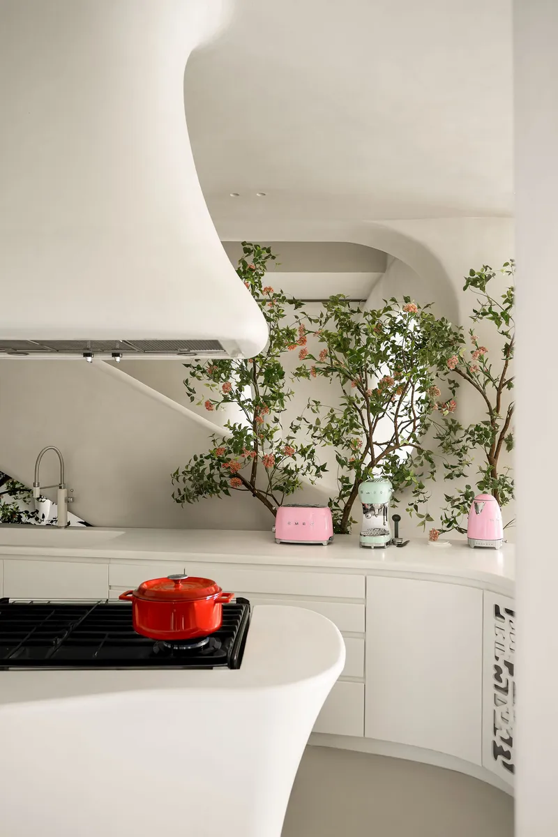 White kitchen with curved island, gas cooktop, and espaliered fruit trees growing along the wall