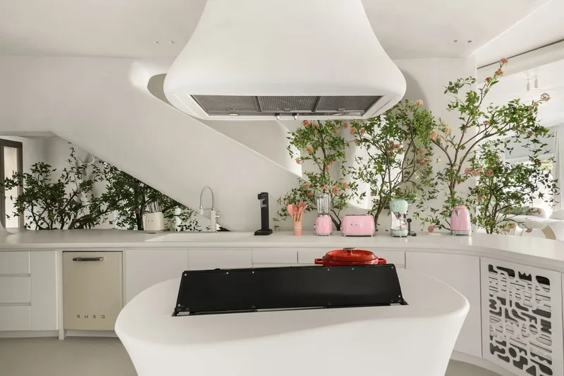 Kitchen island with black cooktop and white countertop lined with potted flowering plants and appliances