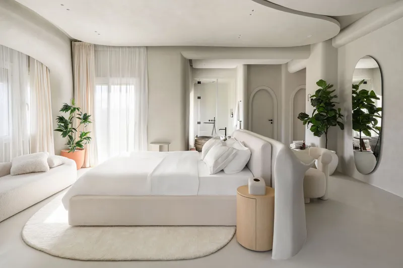 Open bedroom suite with curved ceiling, arched doorways and indoor plants flanking upholstered seating