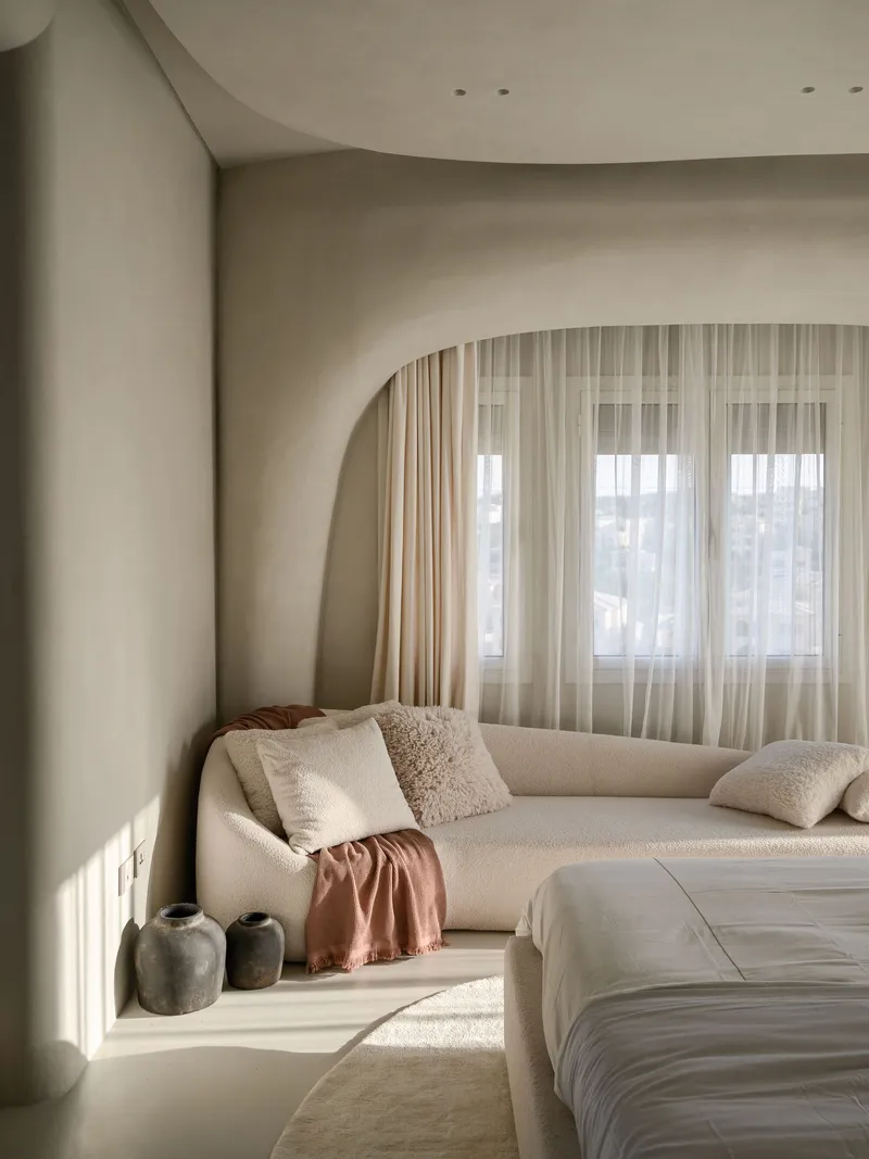 Arched window alcove with built-in daybed receiving warm afternoon sunlight through layered curtains