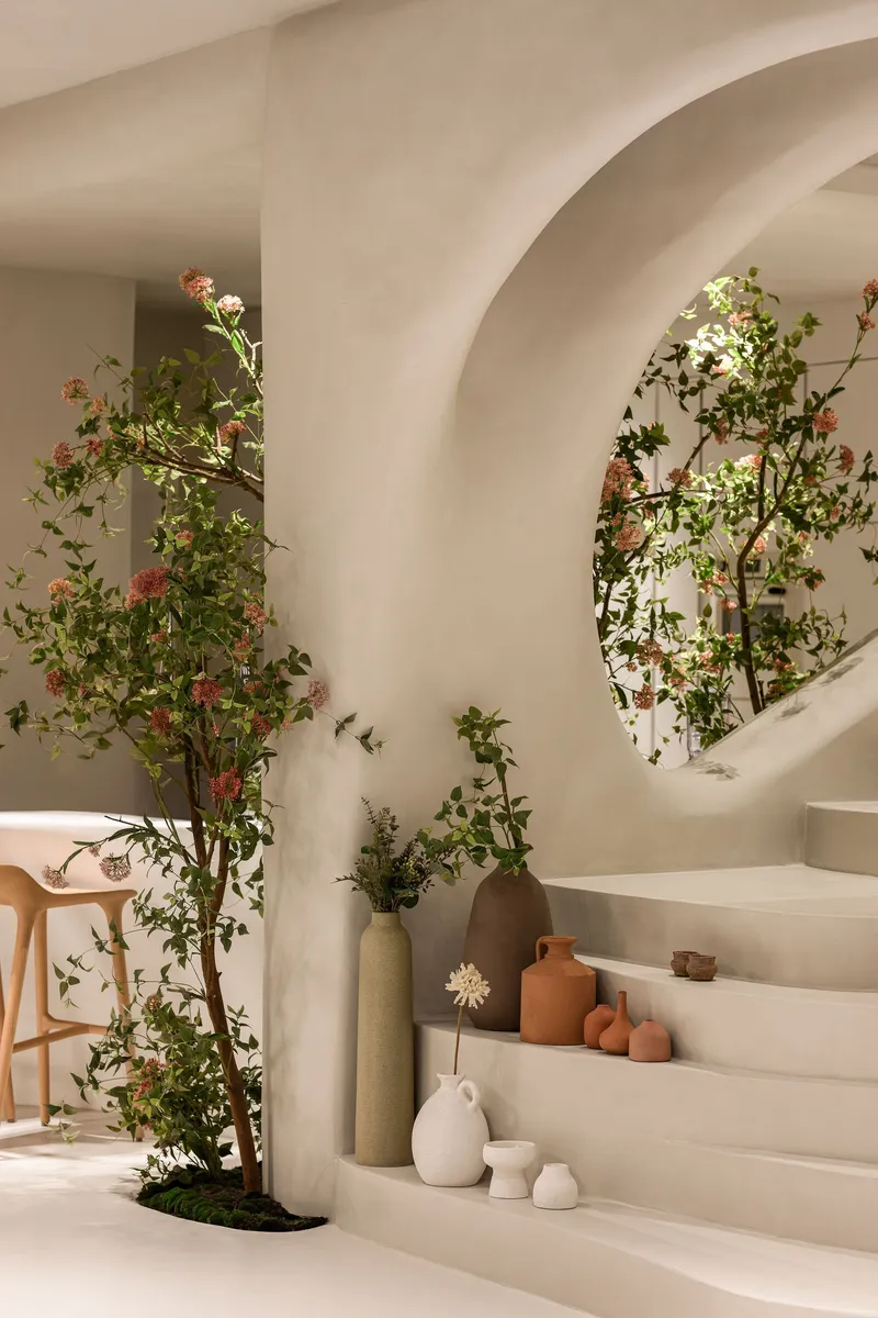 Circular portal framing stepped display shelves with planted tree and ceramic vessels beneath vaulted ceiling
