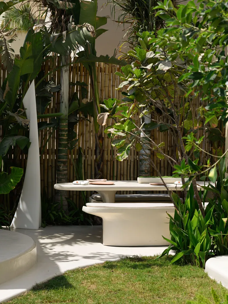 Courtyard seating area with bamboo screen wall and dense tropical planting in dappled sunlight