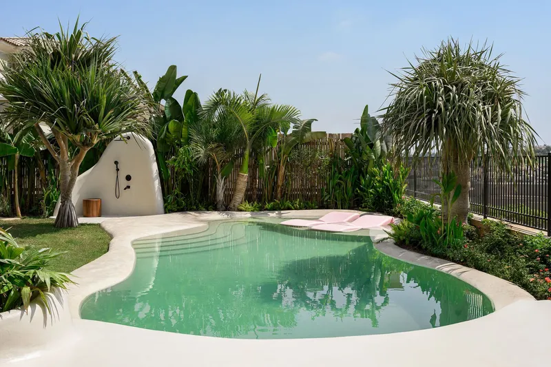 Kidney-shaped pool with pale green water surrounded by lawn and tropical palms under blue sky