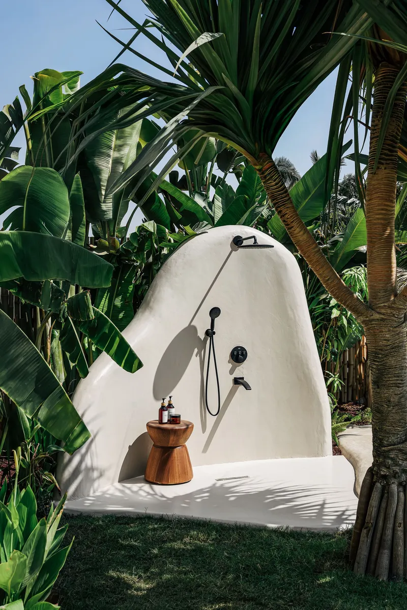 Outdoor shower with curved white plaster wall surrounded by banana palms and tropical plantings