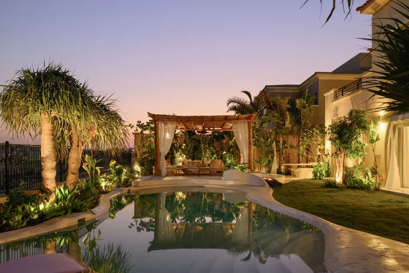 Pool terrace and timber pergola with uplighting among palms at dusk