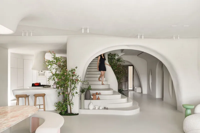 White curved staircase framed by an arched opening with potted trees in the open-plan interior