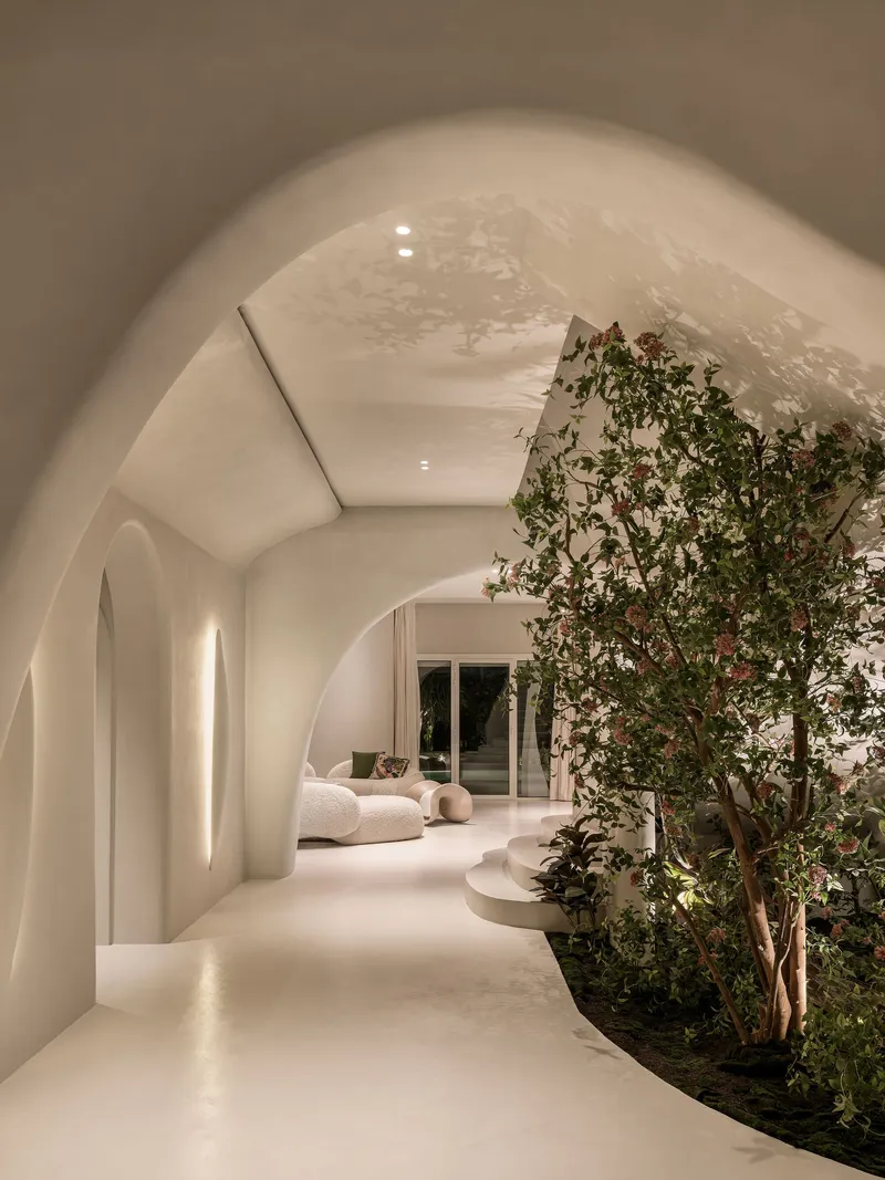 Vaulted corridor with planted trees along one side and warm artificial lighting at night