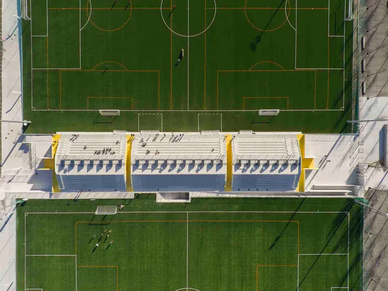 Aerial view of covered bleachers with yellow accents between two synthetic turf football pitches