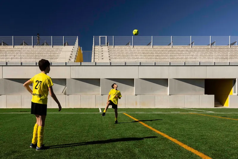 Precast concrete bleacher structure with triangular supports and metal railings overlooking the playing field