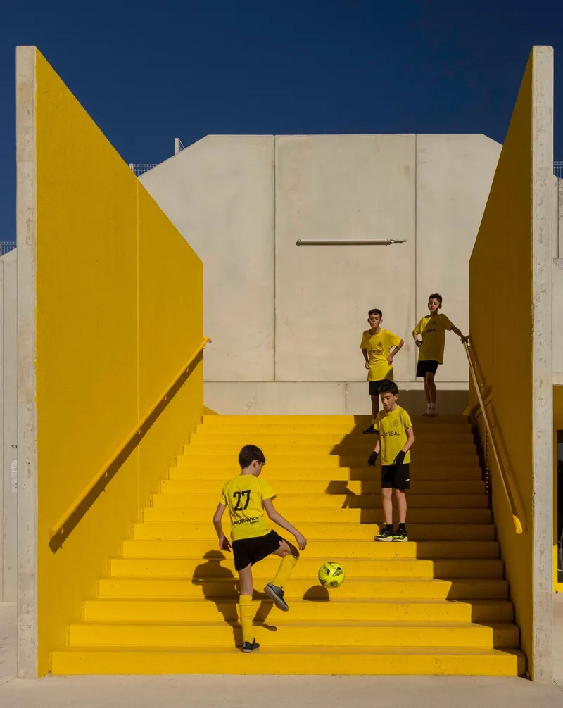 Yellow painted concrete staircase framed by white walls with young players ascending and descending