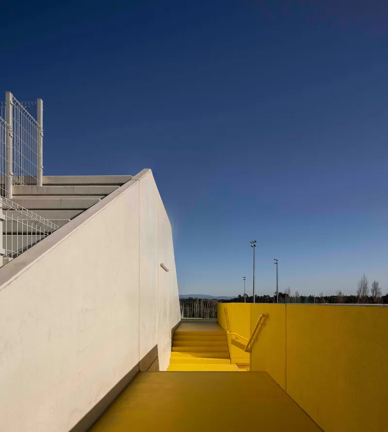 Yellow stairwell descending between white concrete walls under a clear blue sky