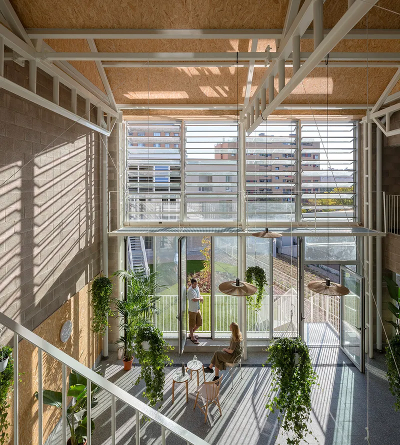 View down into the glazed atrium showing residents and plants on the terrazzo floor below louvered windows