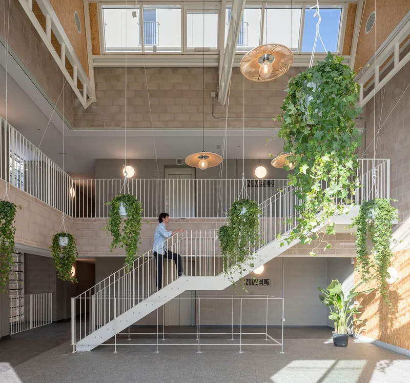 Double-height atrium with suspended planters and a white steel staircase beneath pendant lights