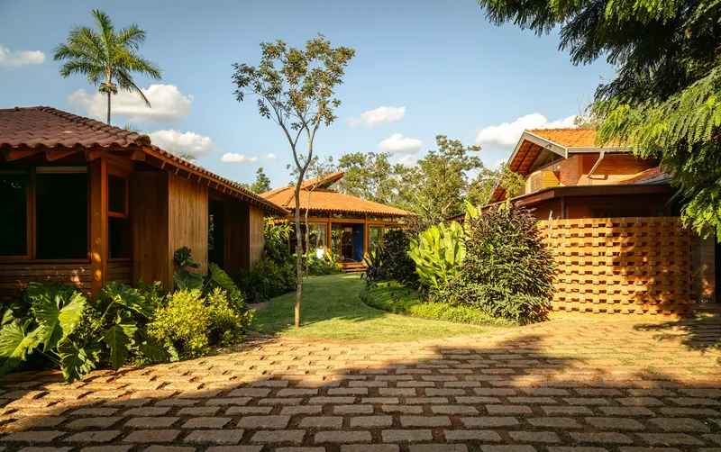 Brick-paved driveway leading through cluster of timber pavilions with terracotta tile roofs and tropical plantings