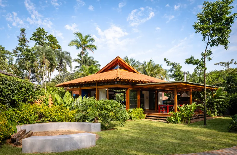 Garden view of open-sided pavilion with terracotta tile roof and concrete bench under palm trees