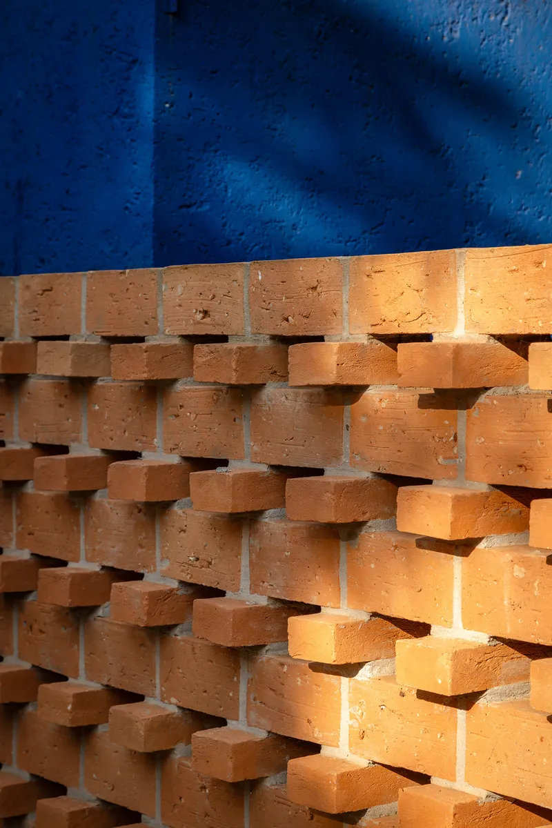 Perforated terracotta brick screen with rounded edges against a blue painted wall in sunlight
