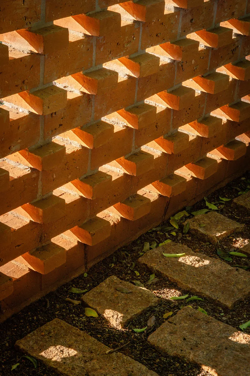 Terracotta brick screen casting diagonal shadows over stone pavers and planted ground below