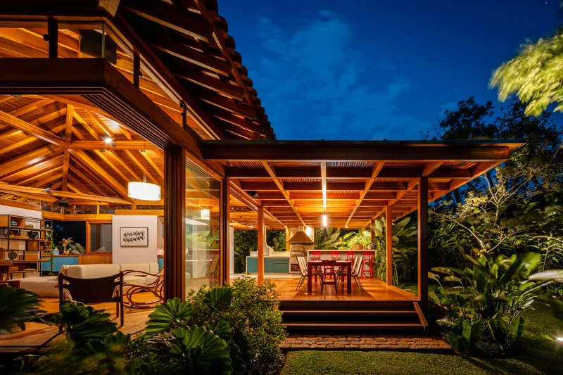 Covered terrace with exposed timber beam ceiling and glazed walls opening to dining area at night