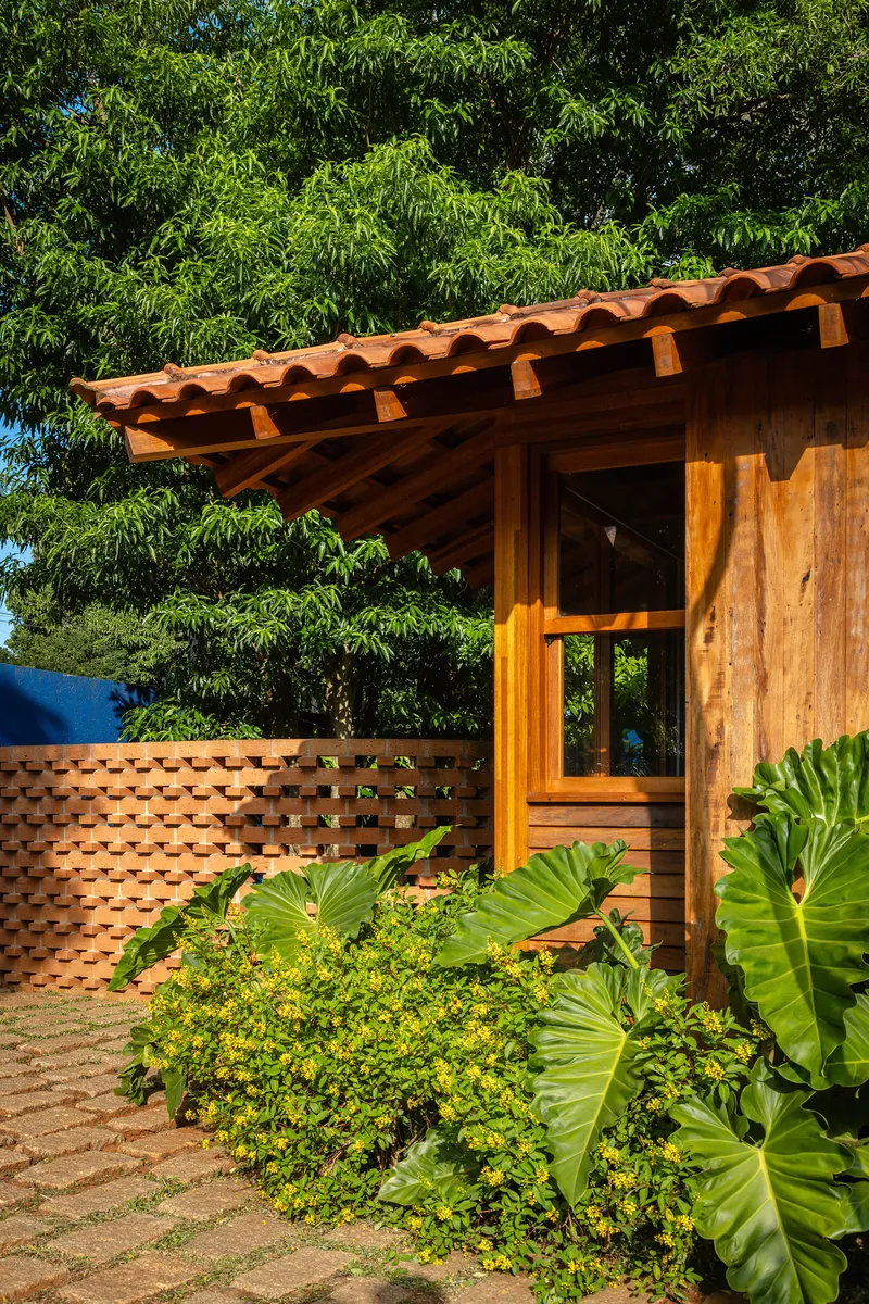 Timber structure with perforated brick screen wall beside planted beds with banana and flowering shrubs