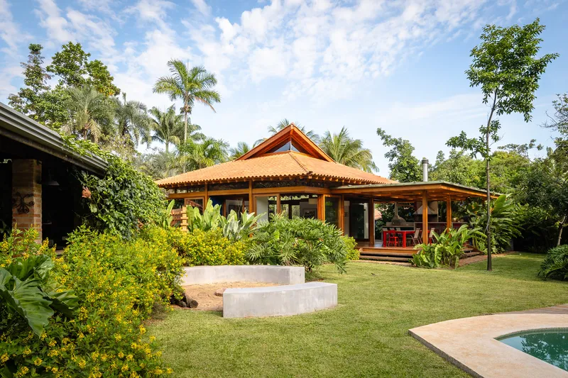 Garden view of open timber pavilion with pitched roof surrounded by palm trees and lawn