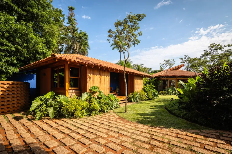 Timber-clad volumes with clay tile roofs connected by patterned paver pathway through garden beds
