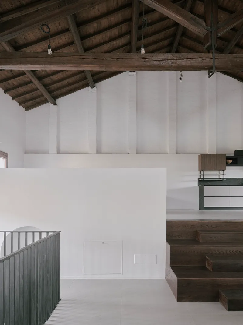 Interior view of dark timber staircase rising beneath exposed wooden roof trusses and white walls
