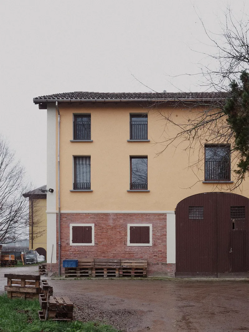 Street facade with yellow plaster upper floors and red brick base beside bare winter trees